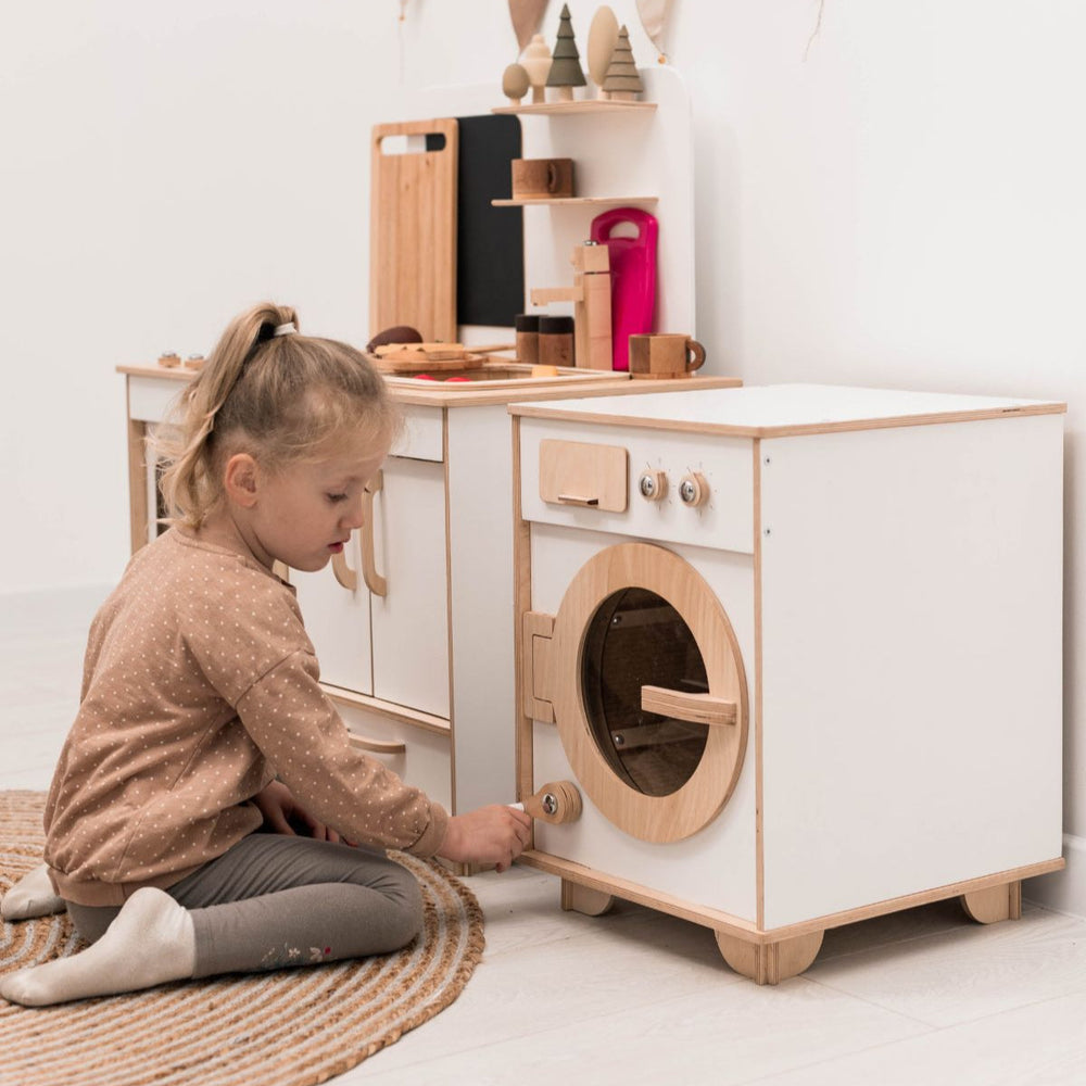 Child playing with a wooden toy washing machine set on a light-colored floor.