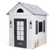 Playhouse with white siding, black door, and decorative elements on a white background