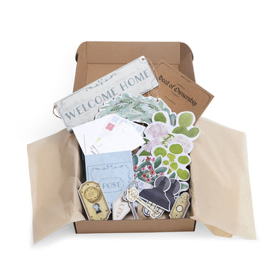 Open cardboard box with decor items including a 'Welcome Home' sign, cards, and decorative elements.