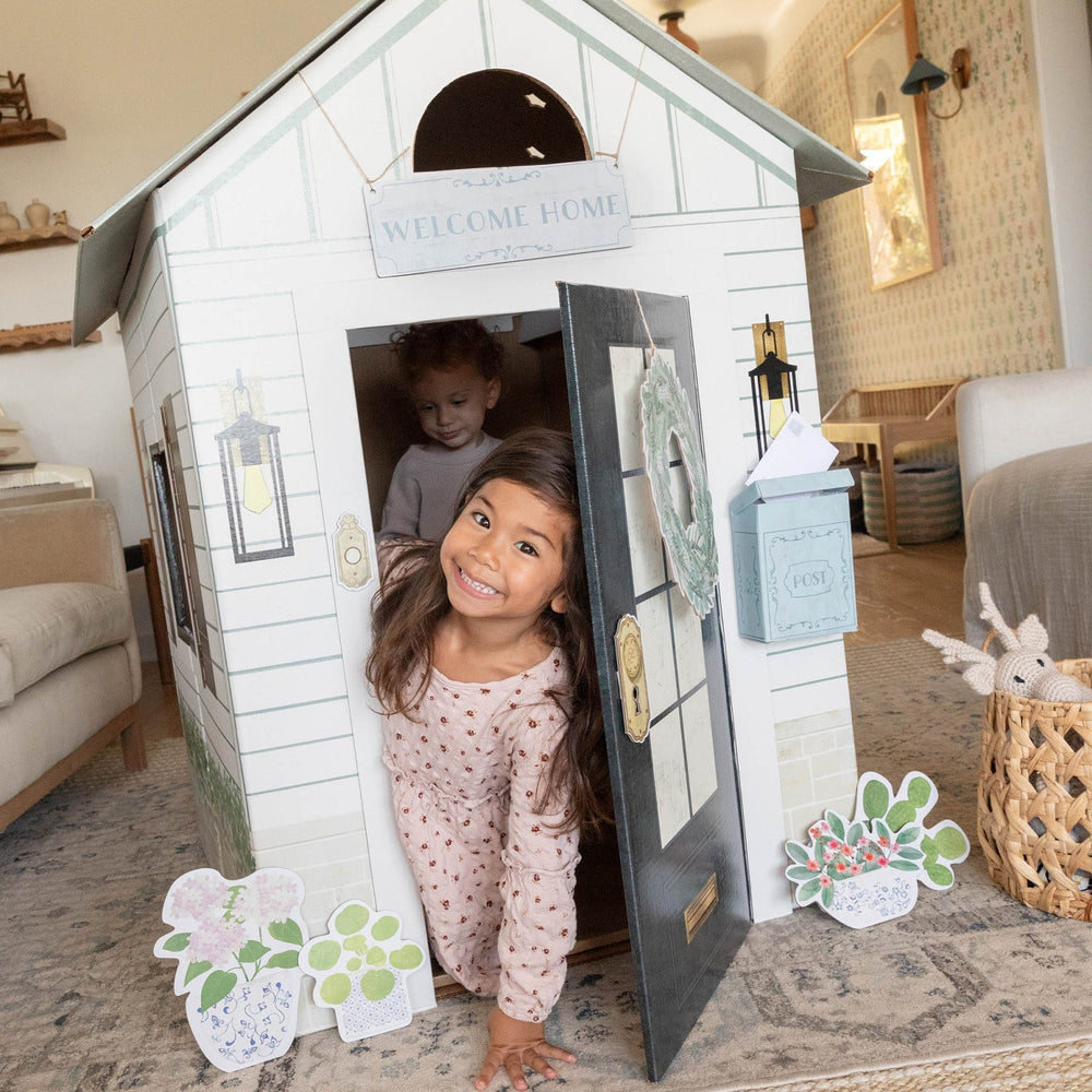 Children playing inside a white playhouse in a cozy living room.