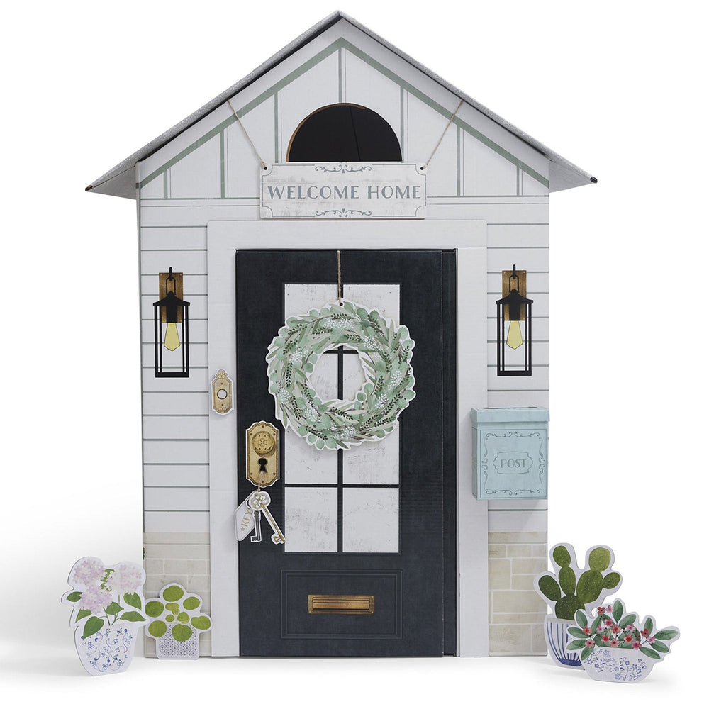 Decorative play house with a wreath on the door, 'Welcome Home' sign, and small plants.
