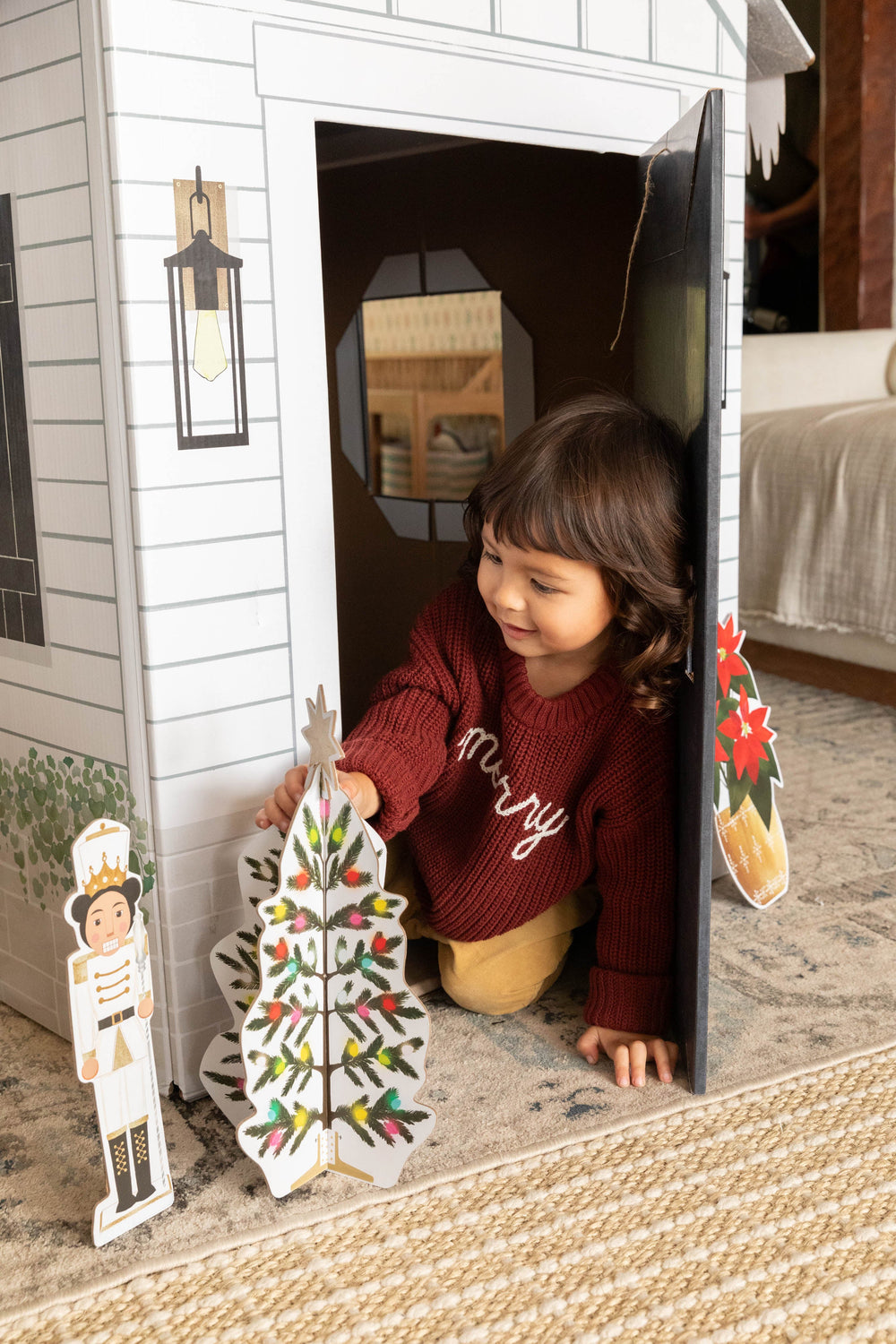 Child playing with a cardboard playhouse in a bedroom