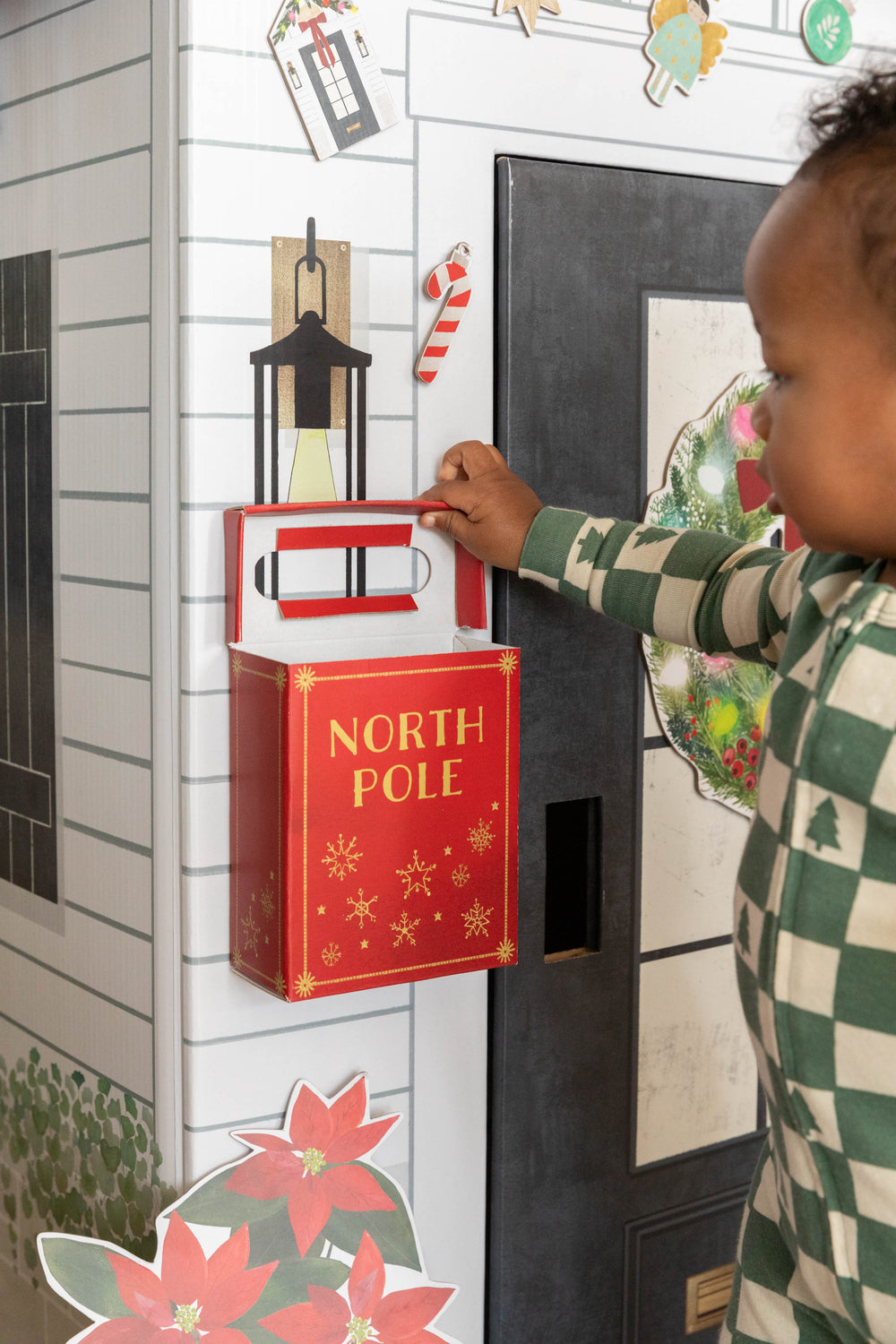 Child interacting with a decorative mailbox labeled 'North Pole' on a festive wall.