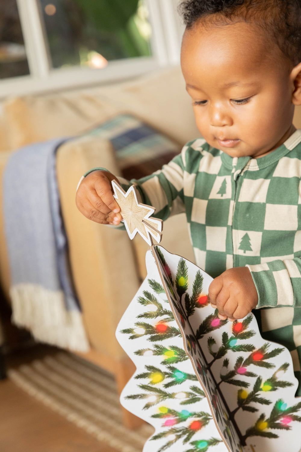 Child holding a Christmas tree-shaped book with a star on a couch
