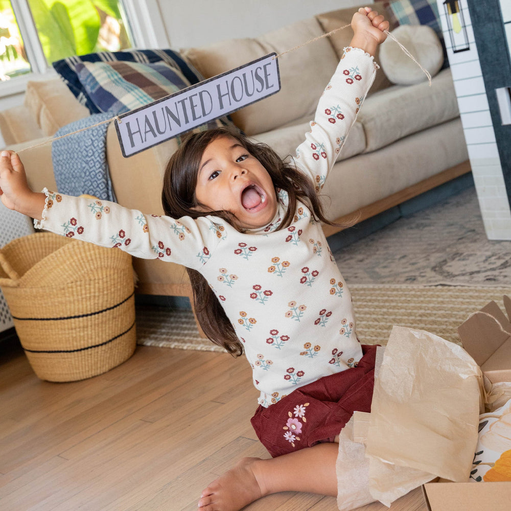 Child playing with a 'Haunted House' sign in a living room.