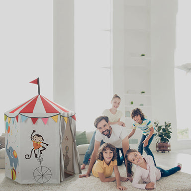 Family playing around a colorful children's play tent in a bright room.