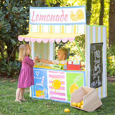 Two children playing with a colorful lemonade stand outdoors.