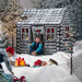 Children playing around a play log cabin in a snowy scene with Christmas decorations.