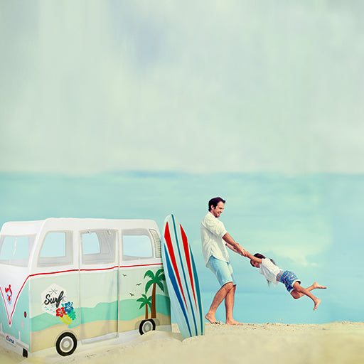 Man and child with a surfboard on a beach near a van play tent.