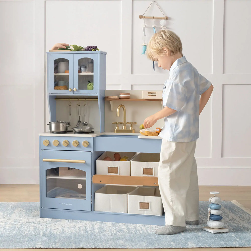 Child playing with a toy kitchen set in a room with light-colored walls.