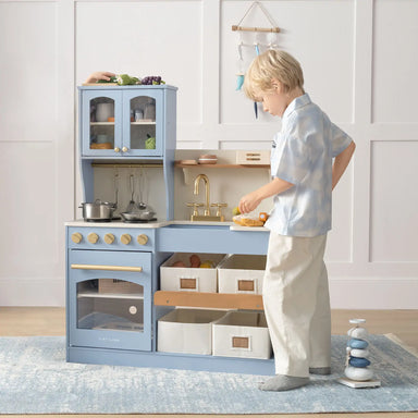 Child playing with a toy kitchen set in a room with light-colored walls.
