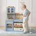Child playing with a toy kitchen set in a room with light-colored walls.