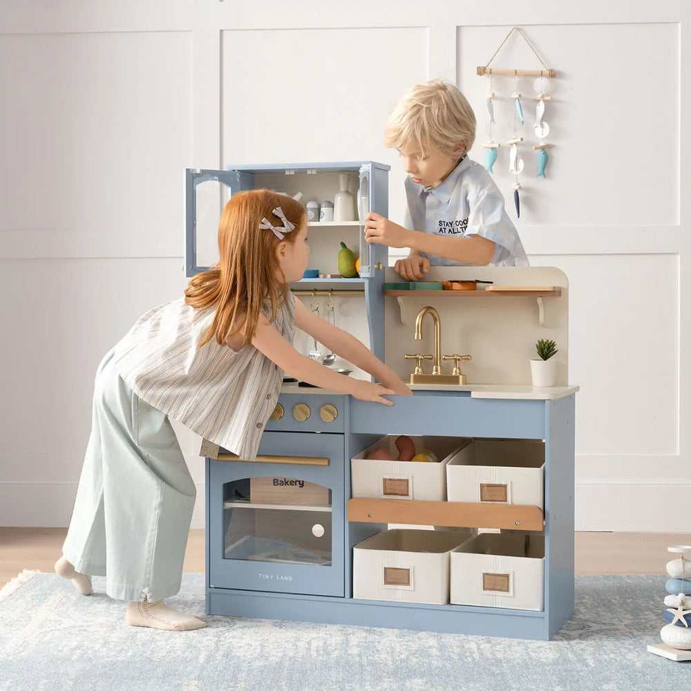 Two children playing with a blue toy kitchen set in a room.