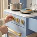 Child playing with a toy kitchen set, turning knobs on a blue stove.