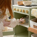 Child playing with a toy kitchen set, interacting with wooden utensils.