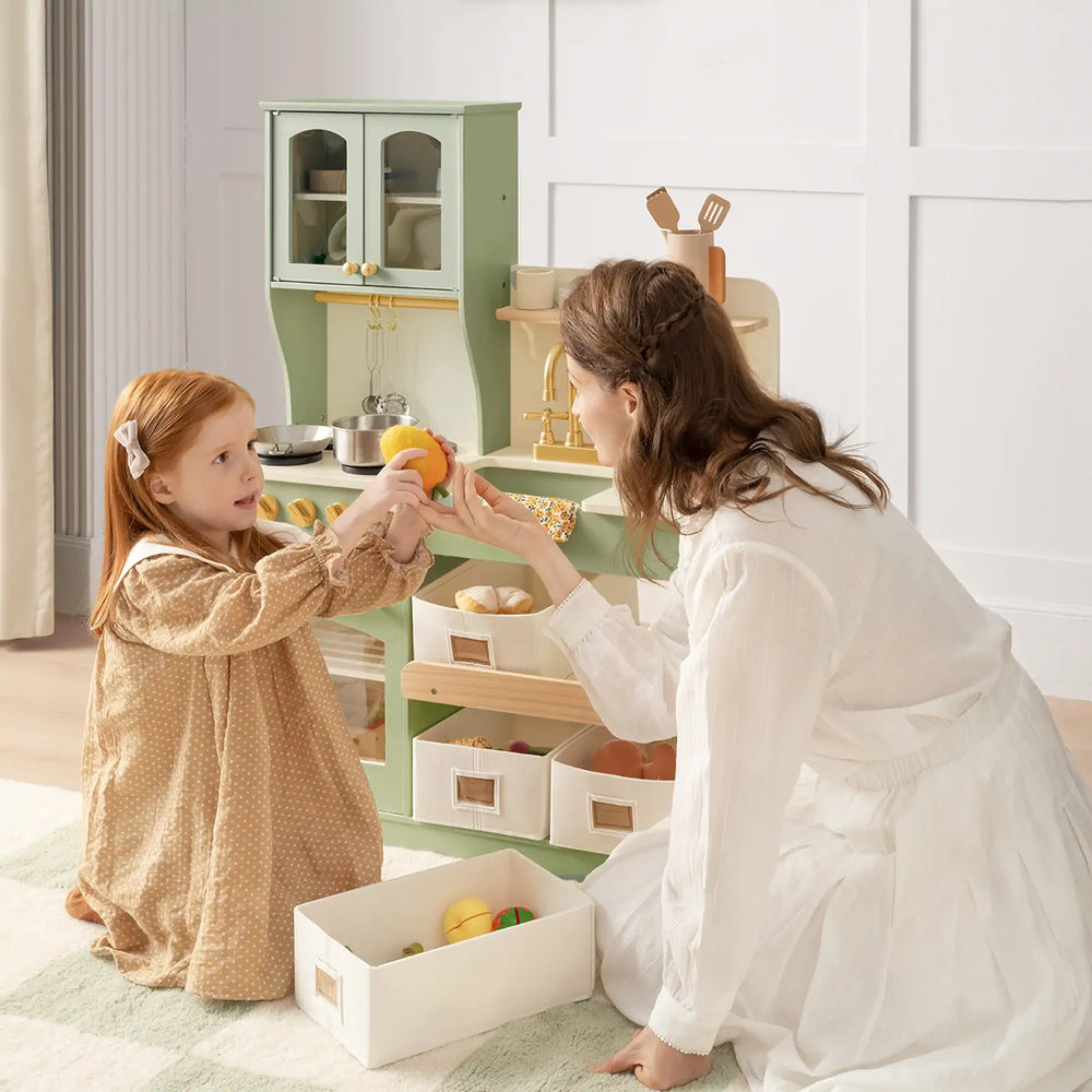 Little girl and her mother playing with food in a green toy kitchen