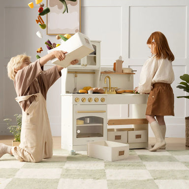 Two children playing with a toy kitchen set in a bright room.