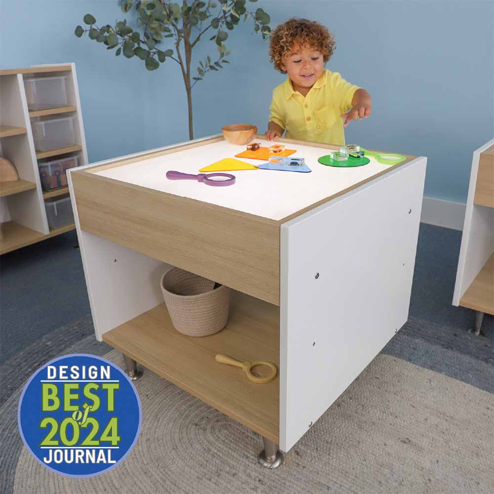 Child playing at a light table with toys in a room setting, featuring the 'Best 2024' design journal badge.