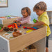 Two children playing with colorful toys at a wooden table in a classroom setting.