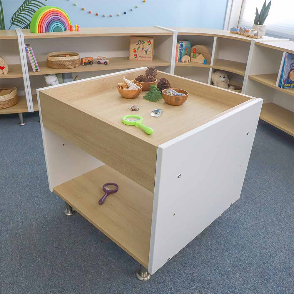 Children's play area with a wooden sensory table and shelves in a classroom setting.