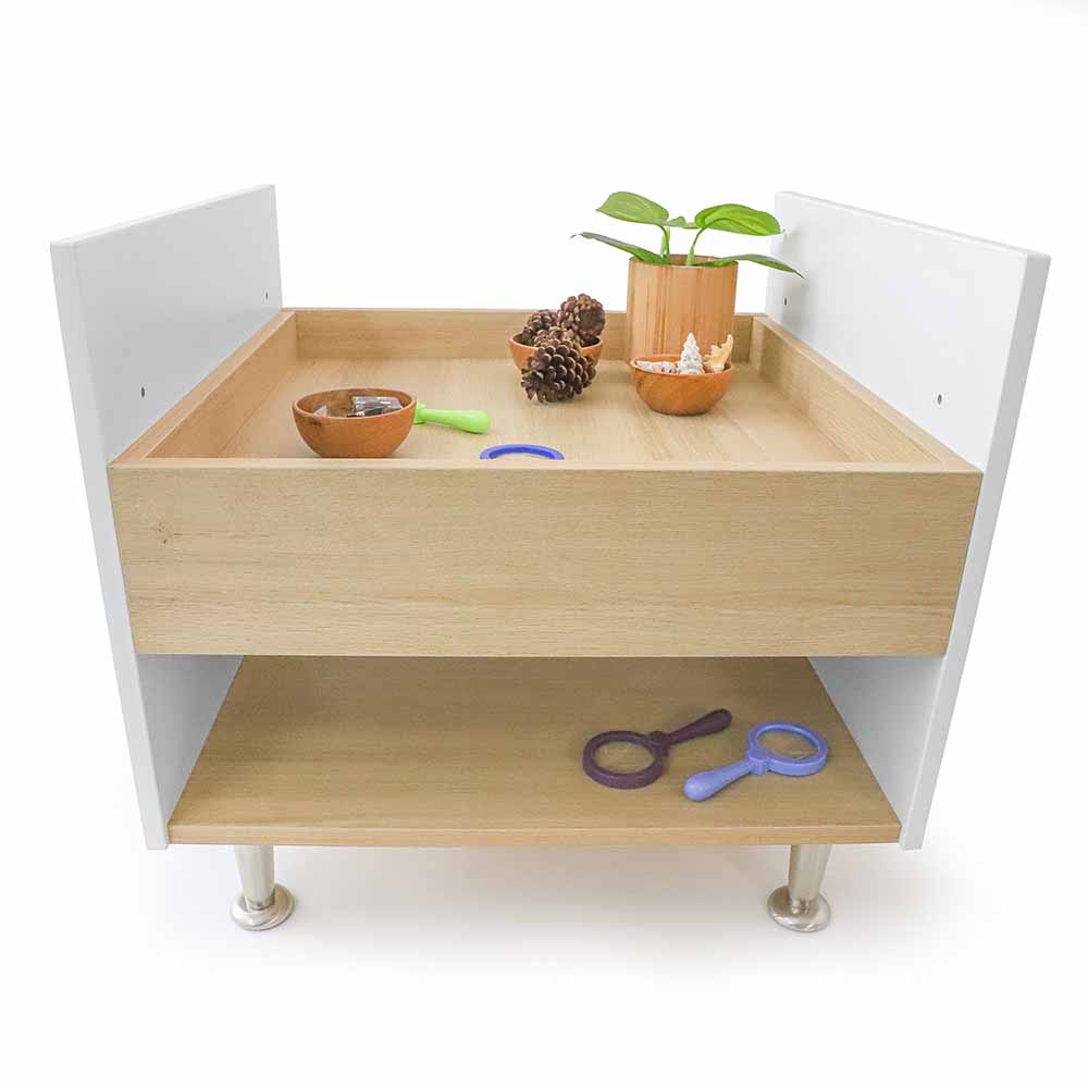 Children's play table with wooden top and white sides, featuring toys and a plant.