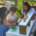 Children and a woman playing with toys at an outdoor play mud kitchen.