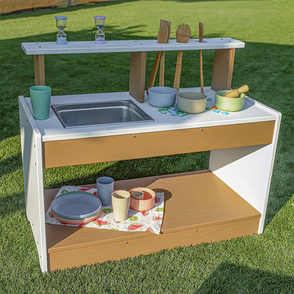 Children's outdoor play mud kitchen set with sink, bowls, and utensils on a grassy background
