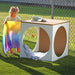 Child playing with a colorful blanket near a wooden outdoor play cube.