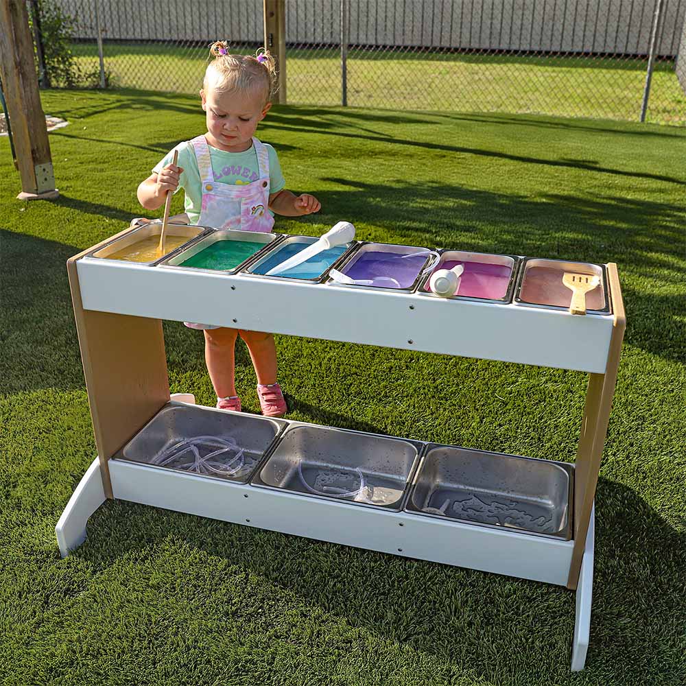 Child playing with a colorful potion station on grass